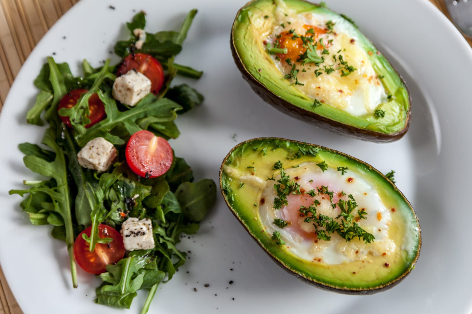 Zapiekane awokado z jajkiem posypane natką pietruszki i sałatka z rukoli, pomidorków koktajlowych i sera feta