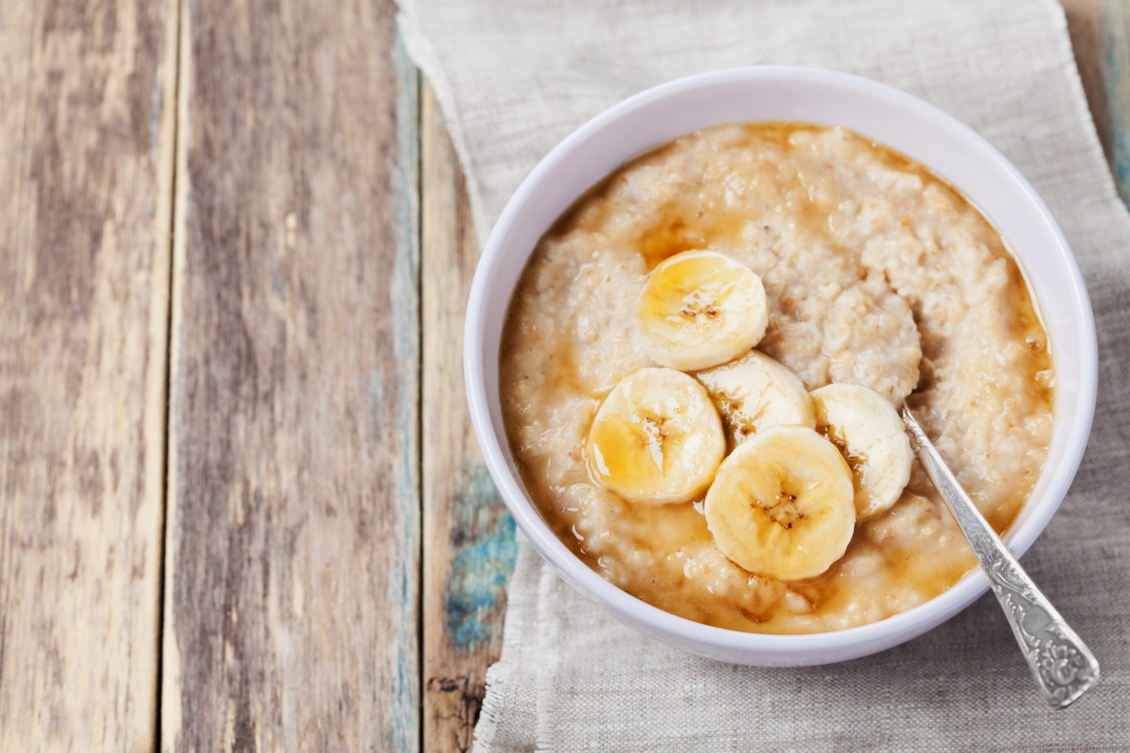 Bowl of oatmeal porridge with banana and caramel sauce on rustic table, hot and healthy breakfast every day, diet food